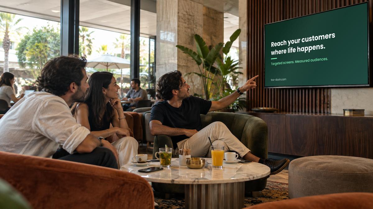 Des amis dans un lounge regardent un écran mural qui diffuse une campagne Toodooh